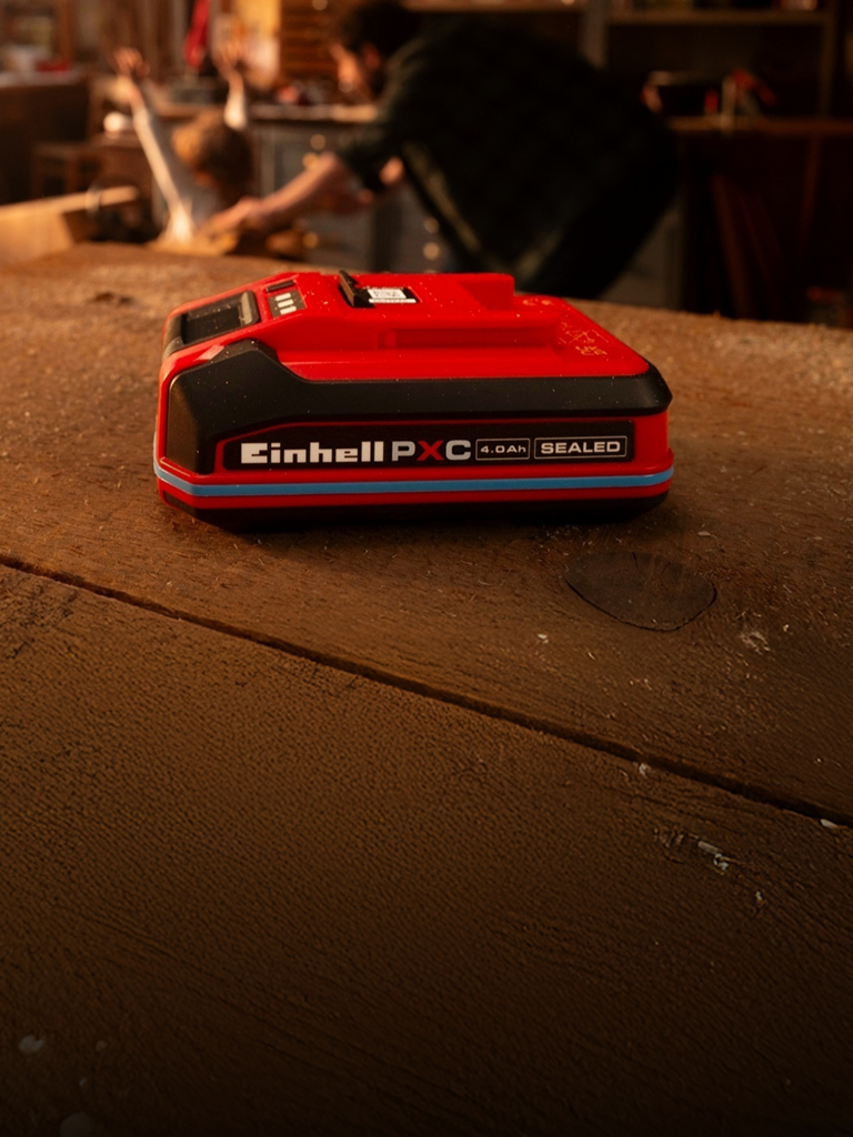 Ahşap bir çalışma tezgahı üzerinde bulunan, mavi halkası ve etiketi görünen Einhell Power X-Change 4.0 Ah SEALEAD akü.