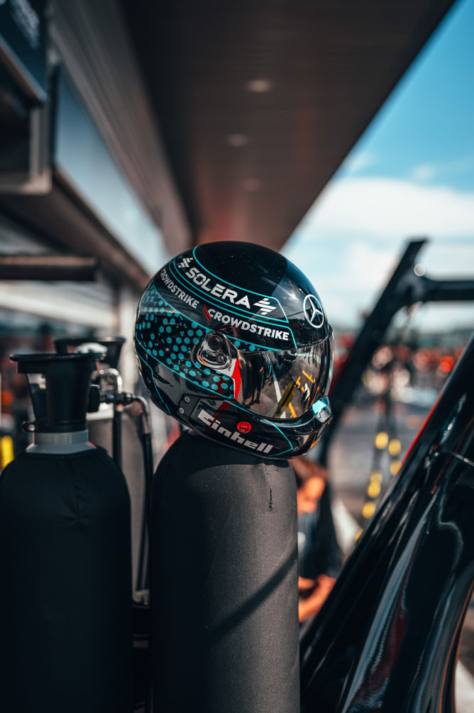 Mercedes-AMG PETRONAS Formula One Team’e ait, üzerinde Einhell, CrowdStrike ve Solera gibi sponsor logoları bulunan bir kask, pit alanındaki bir gaz tüpünün üzerinde duruyor. Vizörün yansımasında garajın çevresi görülüyor.
