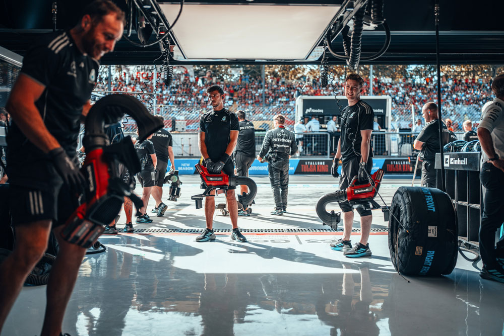 Mercedes-AMG PETRONAS Formula One Team’in mekanikleri, pit stop öncesinde garajda kablosuz Einhell üfleyicilerle hazırlık yapıyor. Arka planda tribünler taraftarlarla dolu.