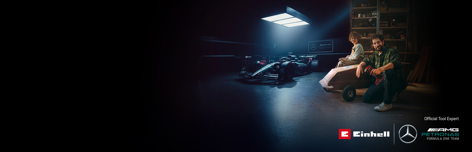 Bir baba ve çocuğu atölyede kendi yaptıkları bir soapbox arabasıyla. Arka planda bir Mercedes-AMG PETRONAS Formula 1 aracı ve Einhell aletleri var.