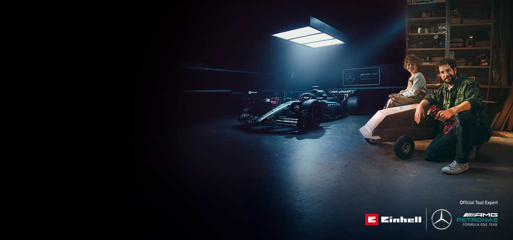 Bir baba ve çocuğu atölyede kendi yaptıkları bir soapbox arabasıyla. Arka planda bir Mercedes-AMG PETRONAS Formula 1 aracı ve Einhell aletleri var.