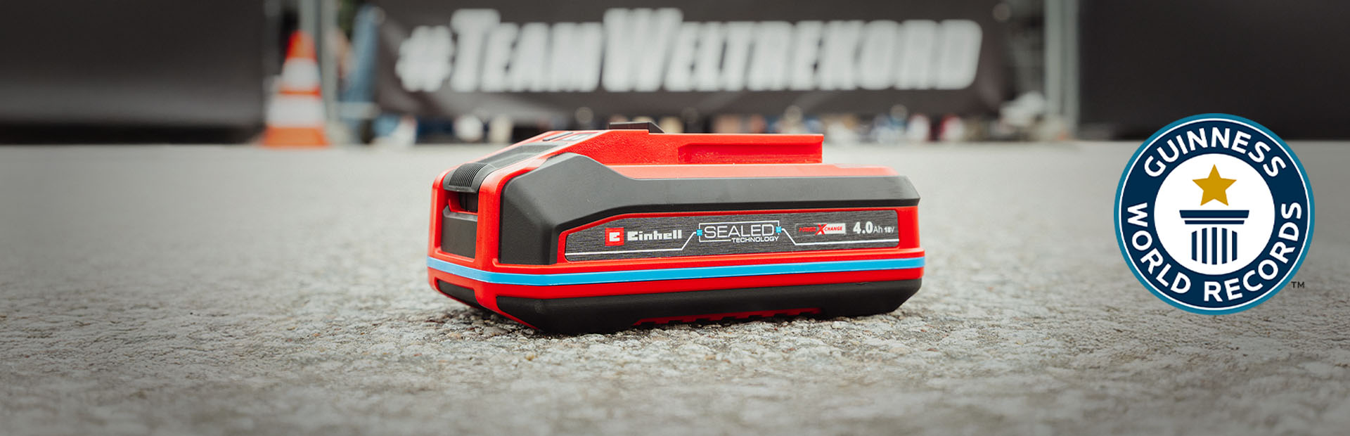 Einhell SEALED akü Power X-Change 4.0 Ah asfalt üzerinde duruyor, sağında Guinness Dünya Rekorları "Rekor Sahibi" logosu bulunuyor.